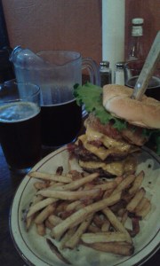 Three patties, layered with cheese and bacon in between, topped with onion rings, lettuce and tomato.